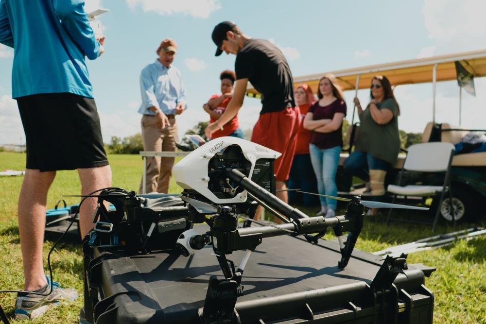 Aviation students working with a faculty member outside with drones over a green landscape